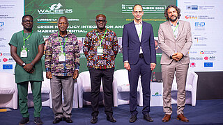 Fünf Referenten stehen auf einem Konferenzpodium.