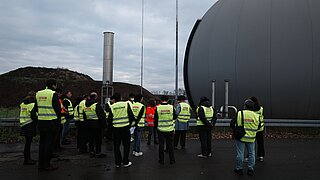 Eine Menschengruppe besichtigt eine industrielle Anlage.