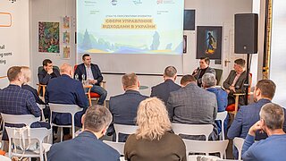 Konferenzteilnehmende sitzen in einem Seminarraum. 