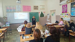 Frauen sitzen in Klassenraum und hören Vortrag einer Frau zu