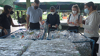 5 Personen mit Gesichtsmasken stehen um komprimierte Blöcke von Plastikflaschen