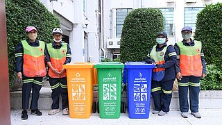 4 Arbeiter stehen neben Mülltonnen zur Mülltrennung
