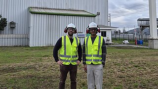 Zwei Männer in Warnwesten stehen vor einer industriellen Anlage.