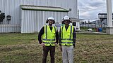 Zwei Männer in Warnwesten stehen vor einer industriellen Anlage.