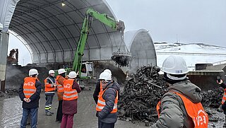 Die Teilnehmenden beobachten, wie ein Bagger mit einem Magneten Metallschrott sortiert.