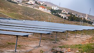 Agri-PV-Anlage auf karger Fläche, im Hintergrund ein Dorf