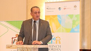 Mann steht an Rednerpult, dahinter Roll-up