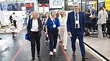 Gruppe von sechs Personen mit Namensschildern geht durch eine Messehalle mit Ständen im Hintergrund
