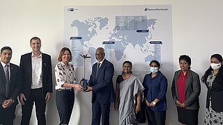 Delegierte der Deutschen Wirtschaft in Sri Lanka, Alexandra Voss (3. v. l) und der Projektleiter Niklas Schiffers (2.v. l.), überreichen dem Water Board einen Mangobaum.