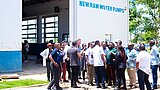 Gruppe von Menschen steht vor einem Gebäude mit der Aufschrift 'NEW RAW WATER PUMPS'