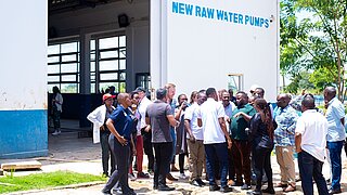 Gruppe von Menschen steht vor einem Gebäude mit der Aufschrift 'NEW RAW WATER PUMPS'