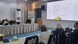 Personen in Konferenzraum mit Präsentation auf Leinwand
