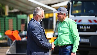 zwei Männer vor Abfallsammelfahrzeug schütteln Hände