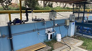 Wasseraufbereitungsanlage mit Rohren, Steuerkasten, Filtern und Schutzdach in einem umzäunten Außenbereich