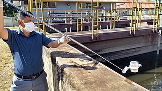 ein Mann mit einer Gesichtsmaske nimmt eine Wasserprobe aus einer Kläranlage
