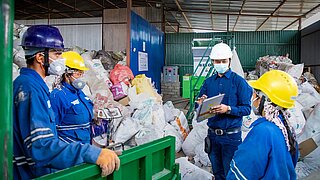 4 Mitarbeiter stehen mit Schutzkleidung, Mundschutz und Helmen in Mülldeponie