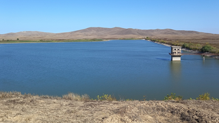 ein großes Wasserreservoir, im Hintergrund eine hügelige Landschaft