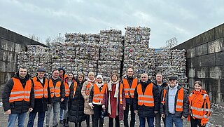 Gruppenfoto der Delegation in einer Recyclinganlage, alle tragen orangene Warnwesten