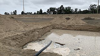 Becken im Sand, in das ein Rohr hängt