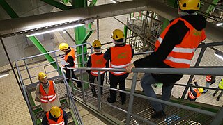 Fünf Personen mit Schutzwesten und Bauhelmen besichtigen ein Werk für Abfallaufbereitung.