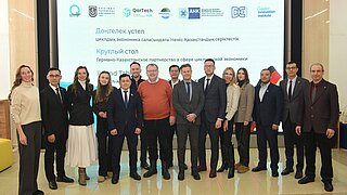 Gruppenfoto mit 15 Personen vor Logowand