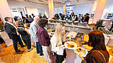 Personen nehmen sich Essen von Buffet oder stehen mit Tellern daneben