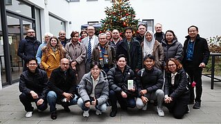 Menschengruppe steht vor einem Weihnachtsbaum.