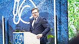 Mann in dunklem Anzug steht hinter einem Rednerpult mit Mikrofon vor einer blauen Wand mit großem weißem Logo und Schriftzug '60 YEARS IFAT'