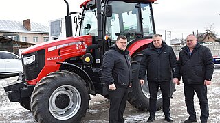 drei Männer stehen vor einem roten Traktor