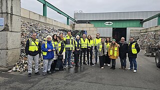 Eine Gruppe steht auf dem Gelände eines Recyclingbetriebes.