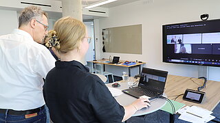 ein Mann und eine Frau nehmen in einem Büroraum an einer Online-Veranstaltung teil