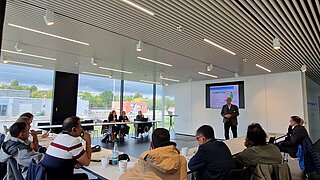 Delegationsgruppe sitzt an Tischen und hört Vortrag zu