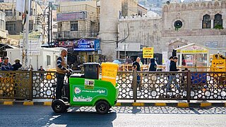 ein Mann fährt auf einem E-Trolley zwei Mülltonnen durch Amman